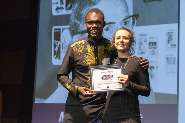 Faculty member and student pose on stage, holding awards.