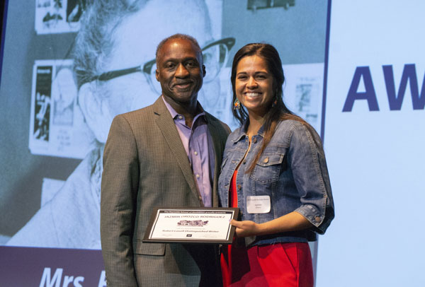 Faculty member and student pose on stage, holding awards.