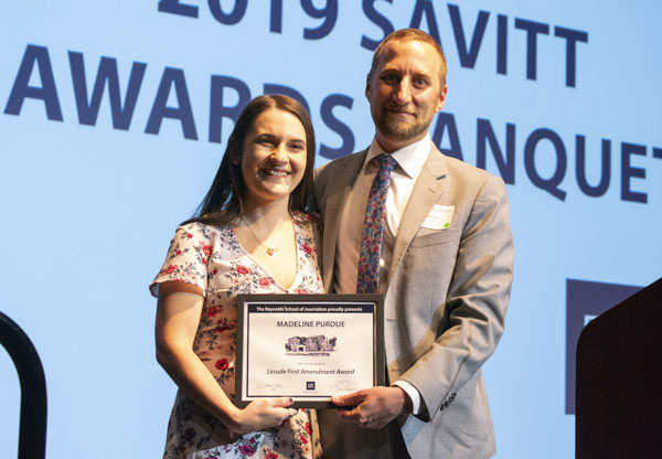 Faculty member and student pose on stage, holding awards.