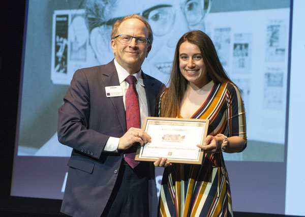 Faculty member and student pose on stage, holding awards.