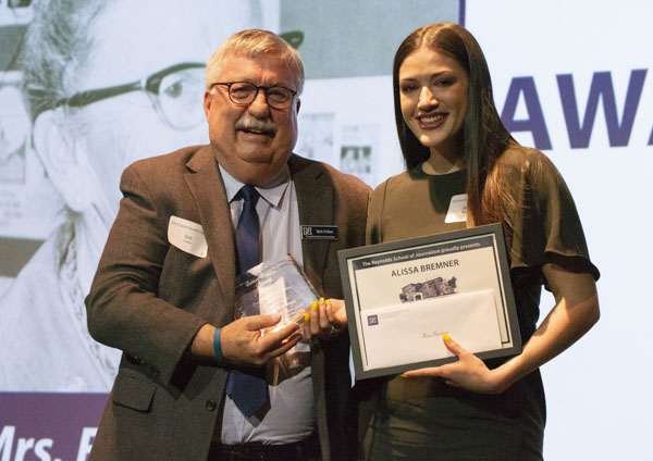 Faculty member and student pose on stage, holding awards.