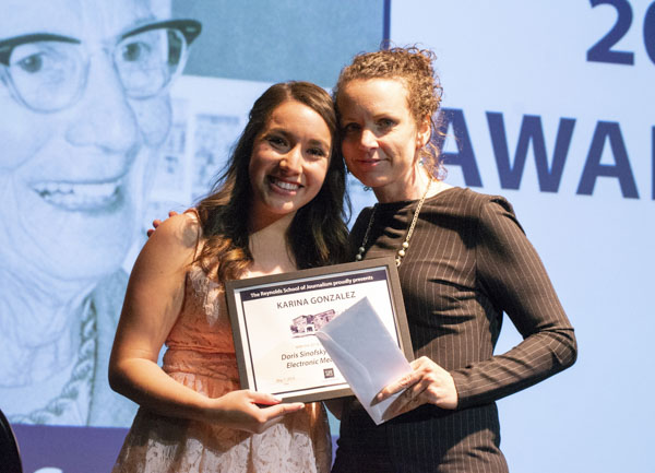 Faculty member and student pose on stage, holding awards.