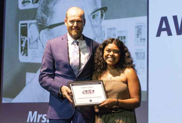 Faculty member and student pose on stage, holding awards.