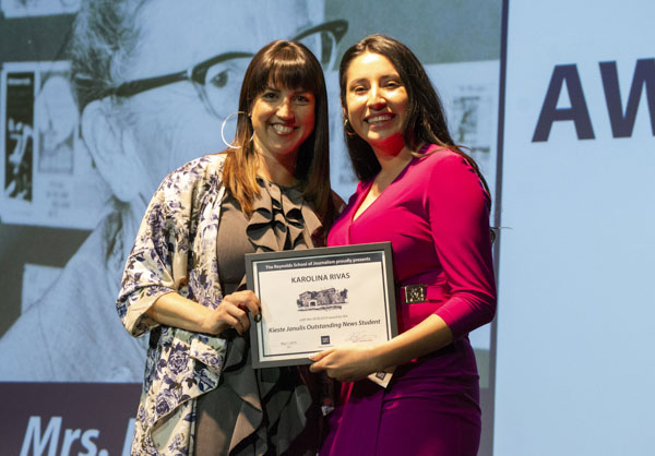 Faculty member and student pose on stage, holding awards.