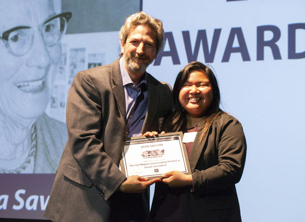 Faculty member and student pose on stage, holding awards.