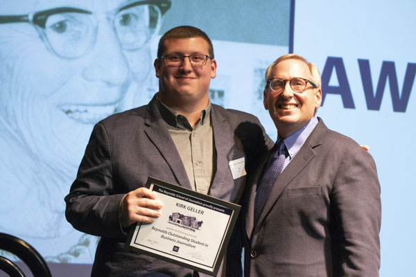 Faculty member and student pose on stage, holding awards.