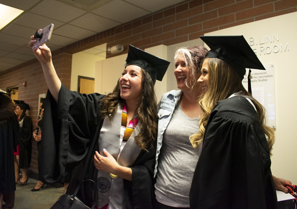 Two students pose with a faculty member for a selfie indoors.