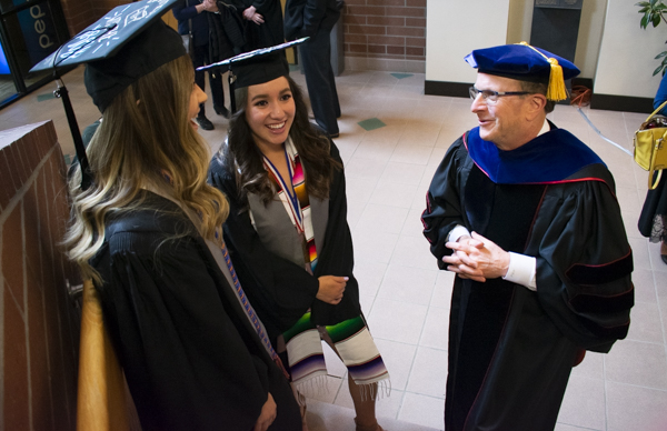 Two students and the dean speak in the atrium.