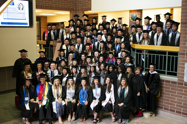 The group of students and faculty pose in regalia for a photo.