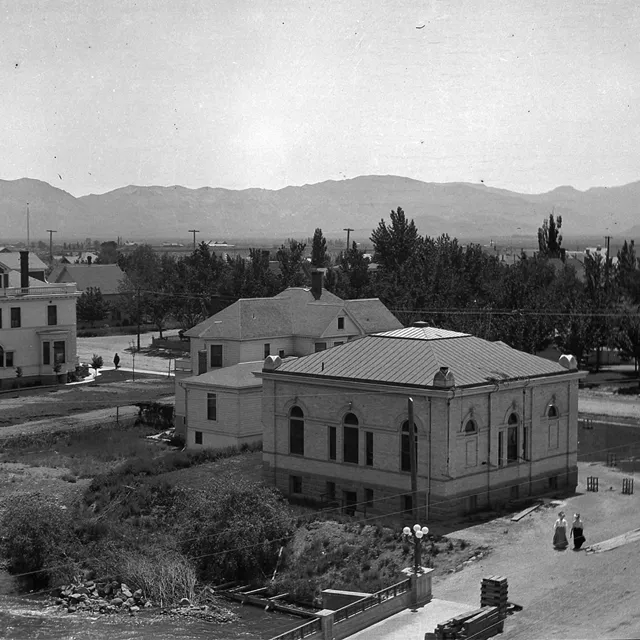 Black and white photo from the 1900s of Reno, a collection of wooden buildings, surrounded by trees, with the Sierra Mountain Range visible in the distance.