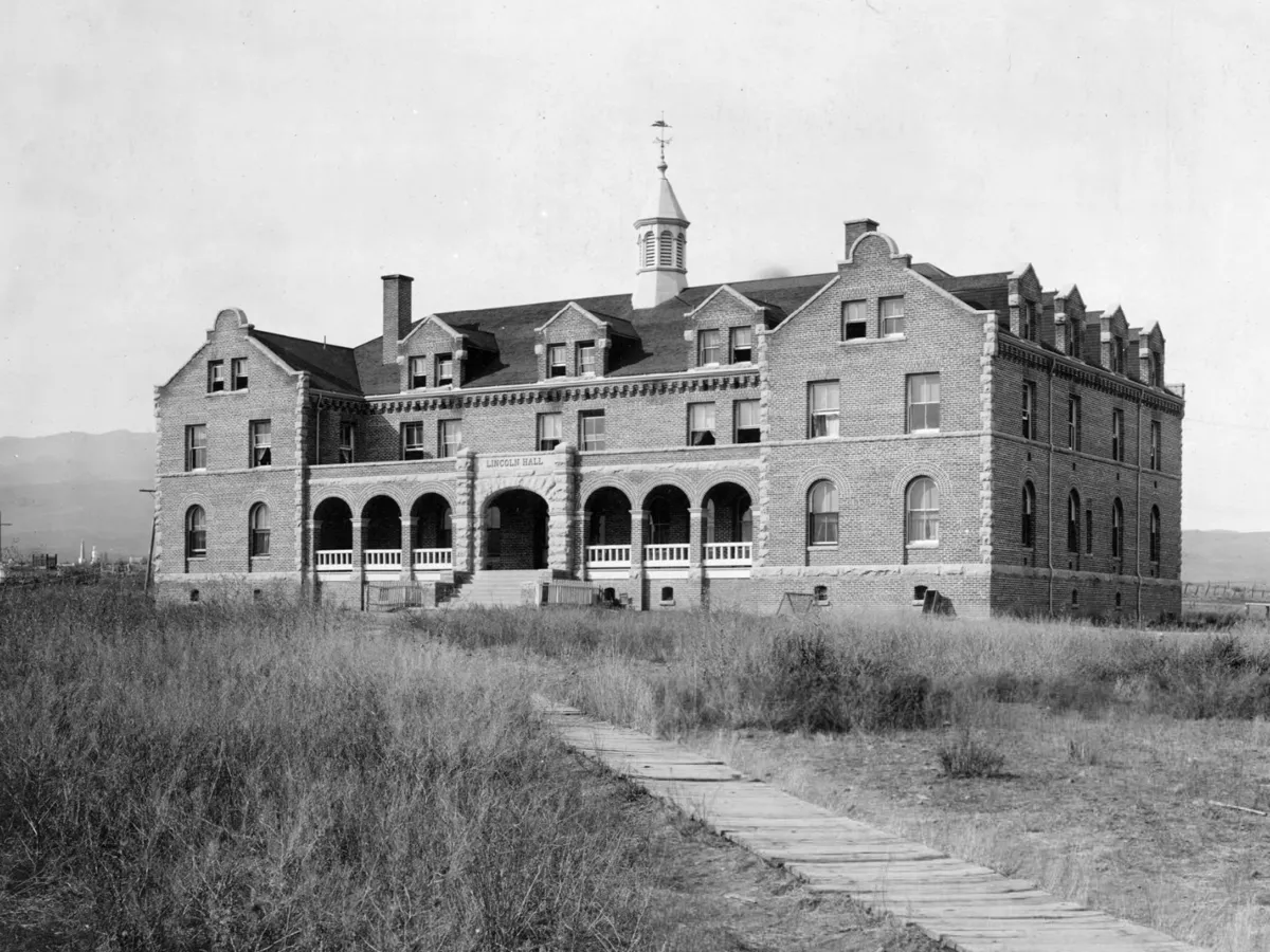 Black and white photograph of Lincoln Hall from 1896, with a wooden boardwalk leading through grassy areas up to the entrance.