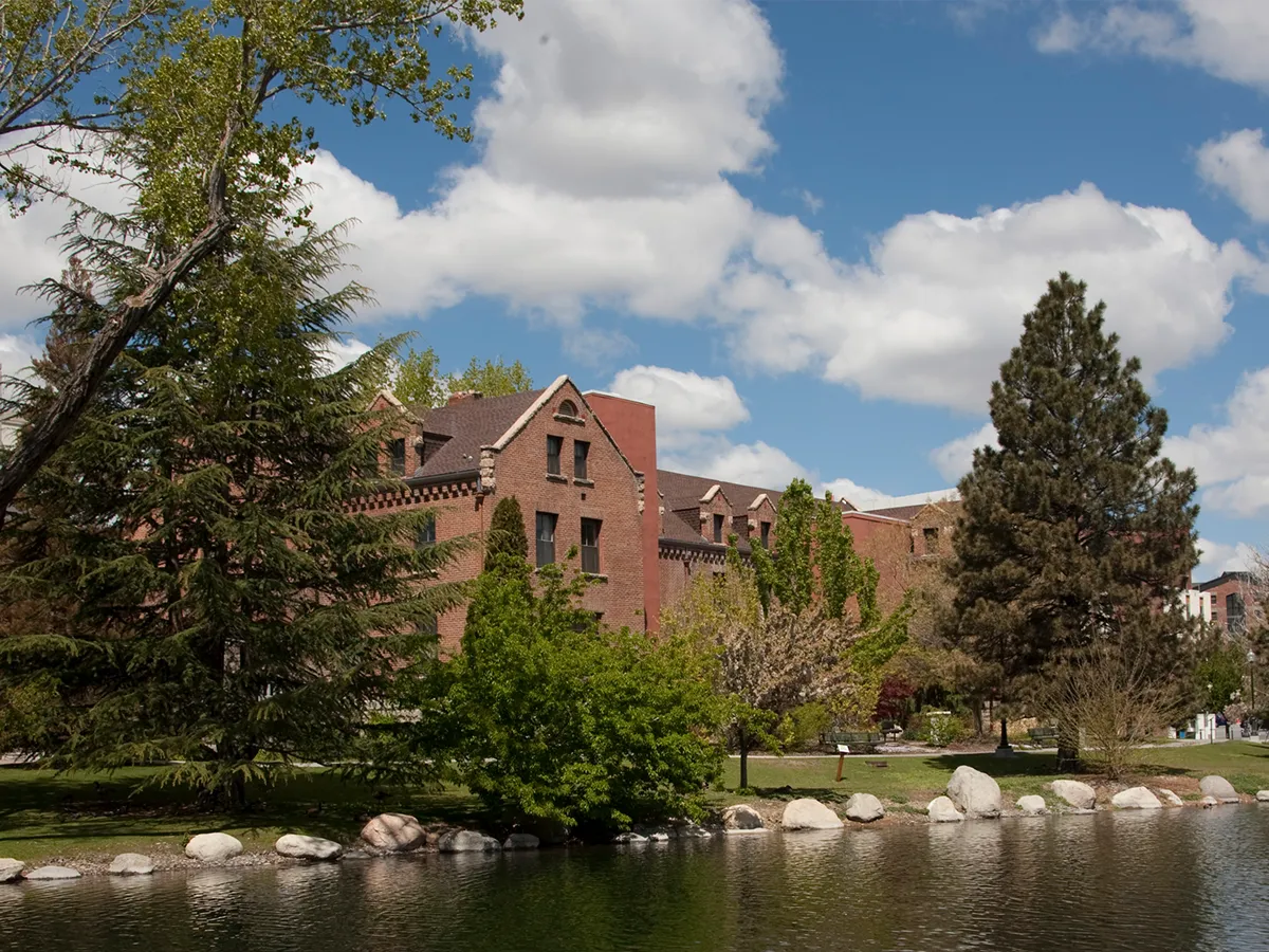Manzanita Hall, flanked by large green trees, sits along Manzanita Lake on the University of Nevada, Reno campus.