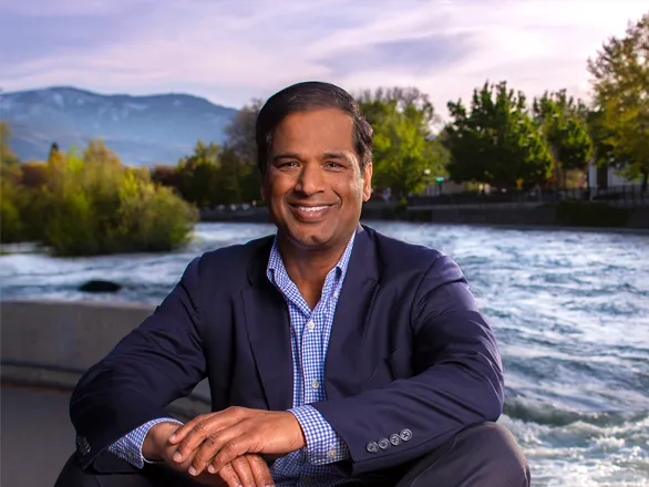 Krishna Pagilla poses for a picture while seated next to the Truckee River with trees surrounding the river behind him.