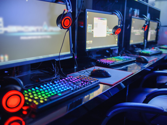 Row of gaming PCs with monitors, RGB keyboards, mice, and headsets set up in an esports lab.