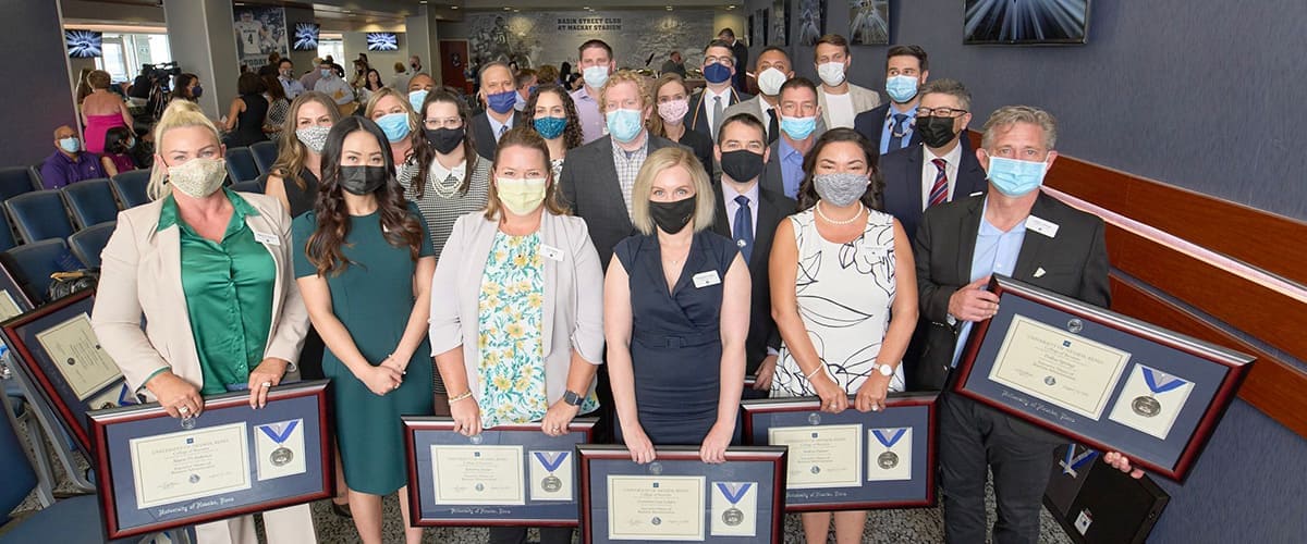 The 2021 EMBA cohort gathers for a photo, holding their degree plaques and wearing face masks. 