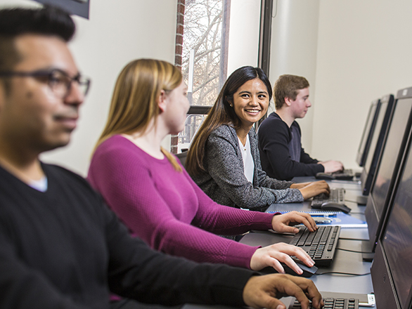Four students sit at a bank of computers working on assignments for Information Systems.