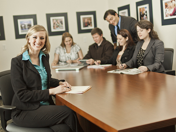 A person in professional attire smiles before giving a presentation to five other people.