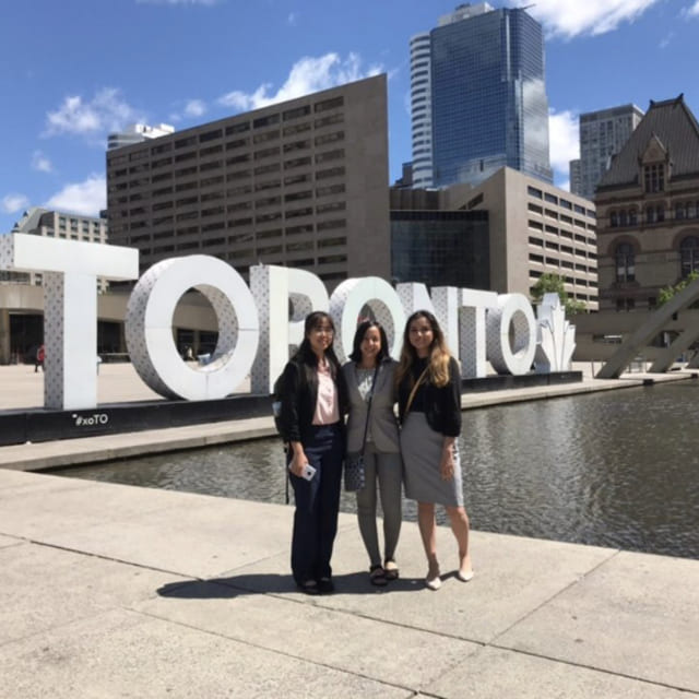 Three students in business attire standing in front of Toronto sign.