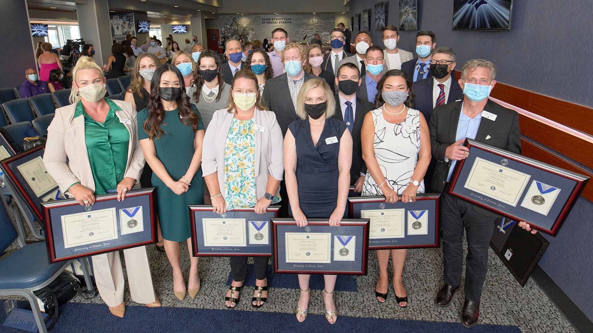2021 EMBA cohort wearing face masks and holding their graduation plaques. 