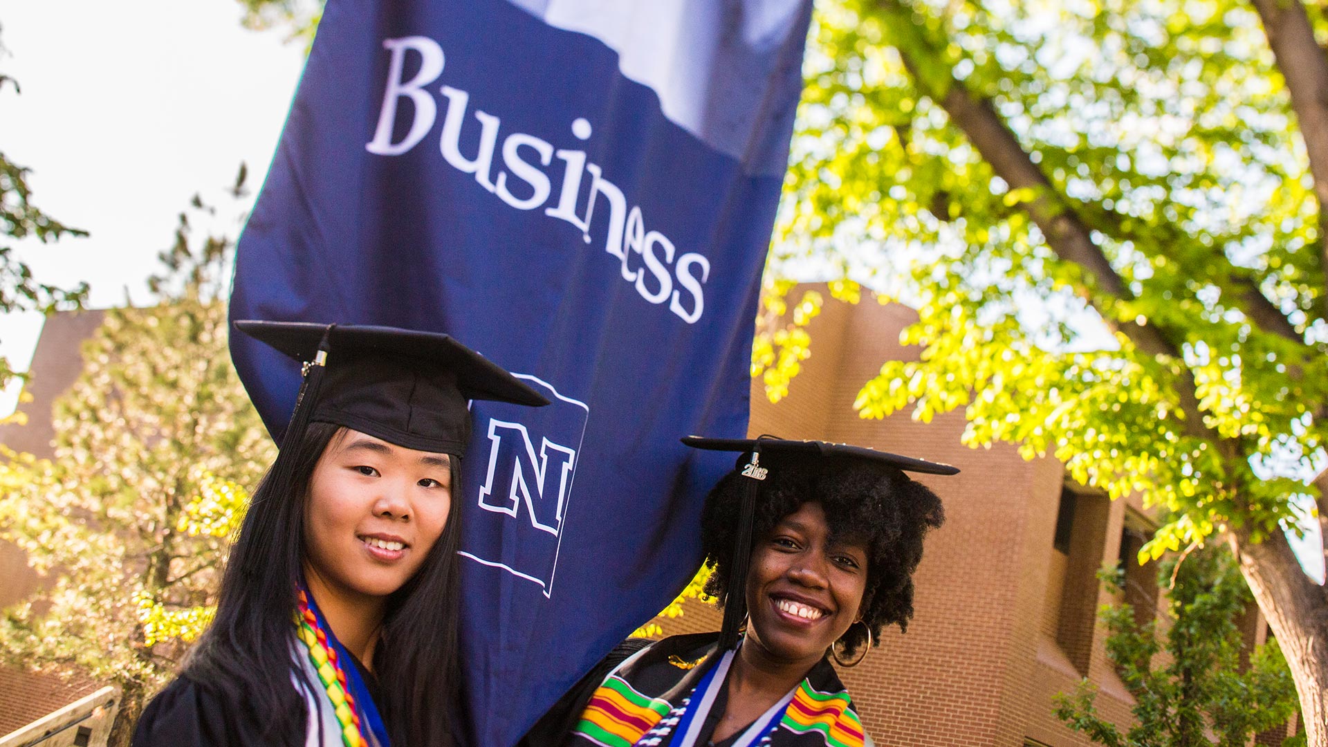 Graduates next to a banner for the College of Business at commencement