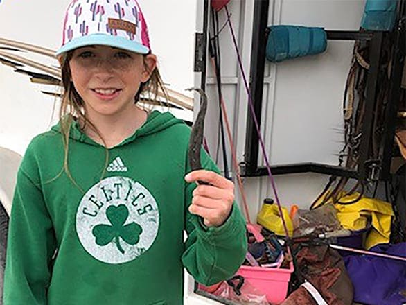 4-H'er Hannah in a ballcap and green clover hoodie poses with hoof pick.