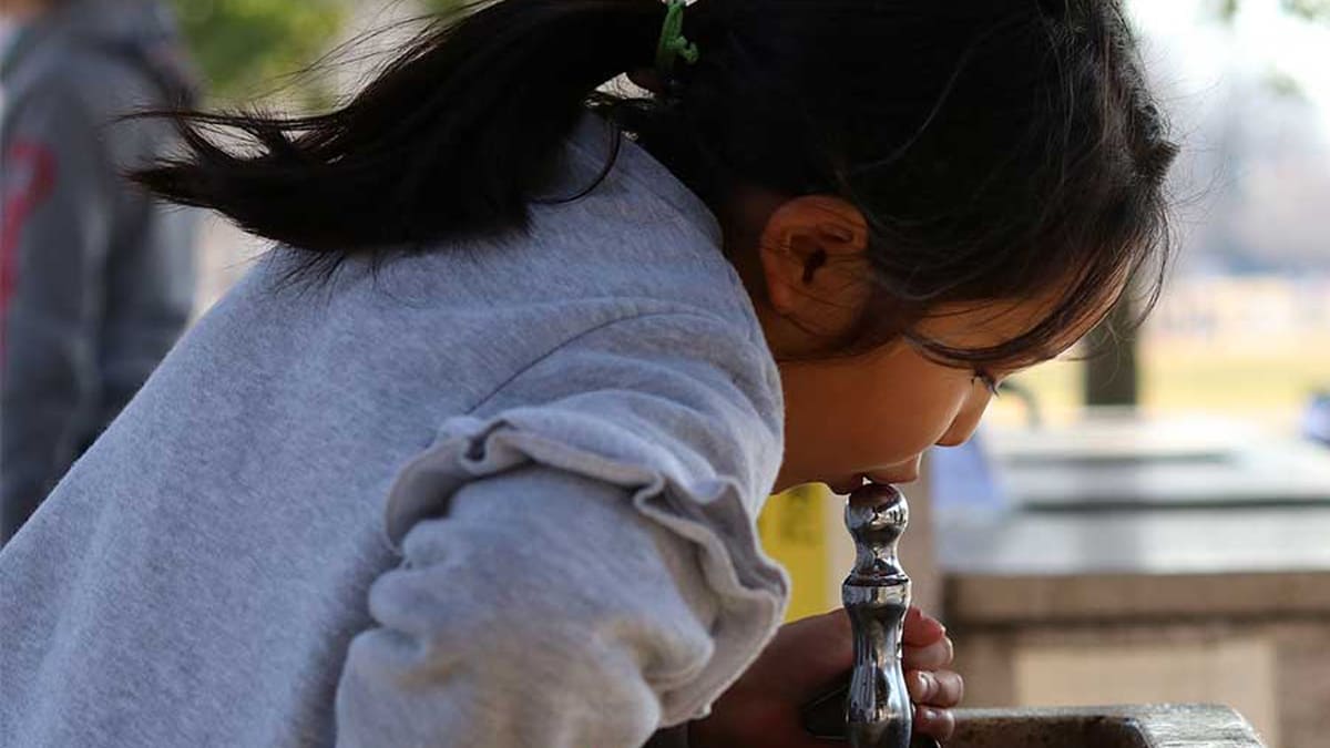 Girl drinking from a park's water fountain