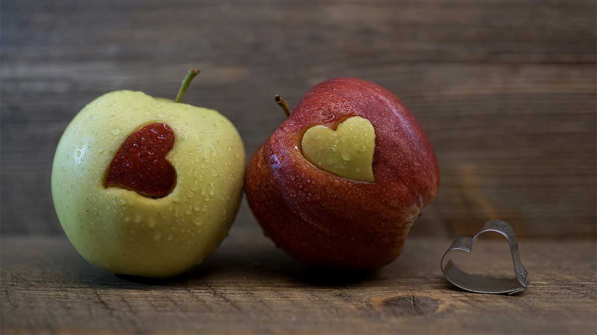 A red and green apple with a heart-shaped cut-out of each in the other
