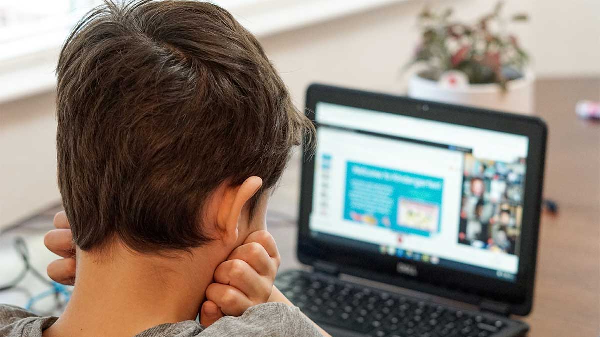 Kindergartener using a laptop at the kitchen table to attend school virtually