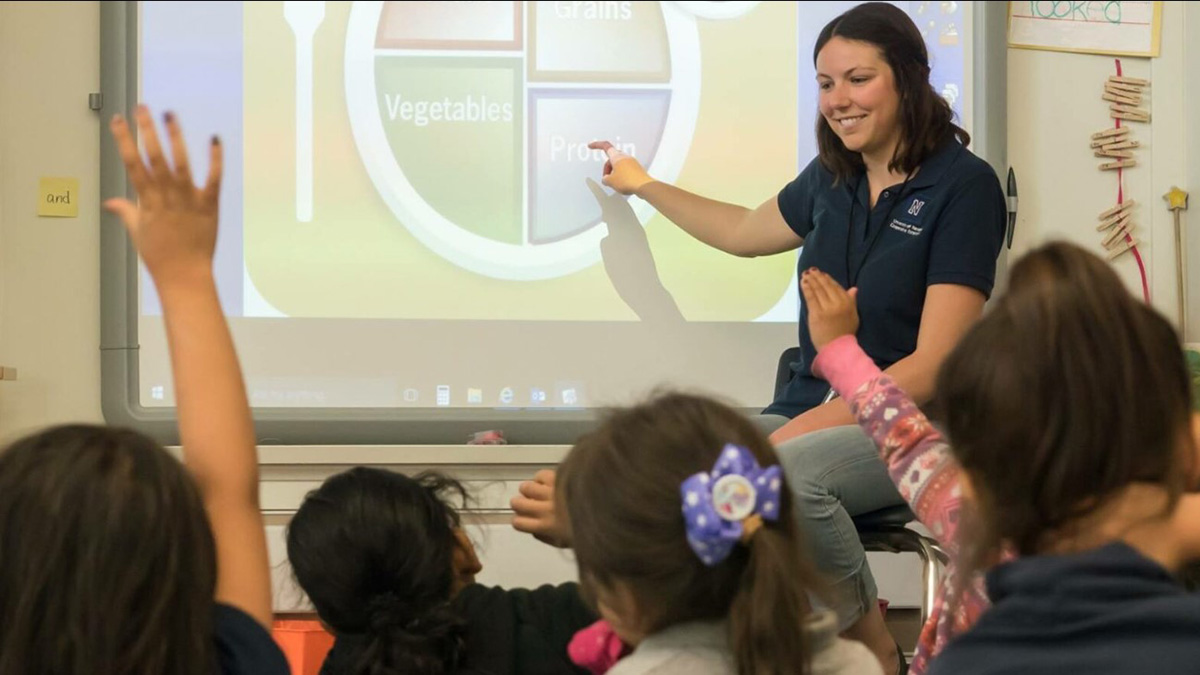 An Extension instructor pointing to the protein section of the MyPlate graphic as students raise their hands