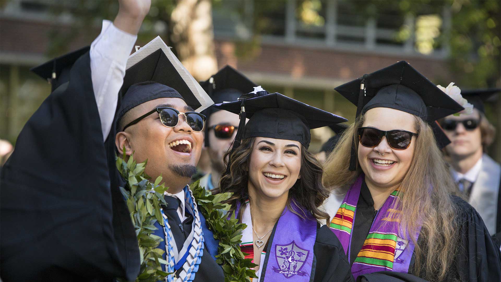 Three smiling graduates in decorated caps and gowns celebrating at commencement