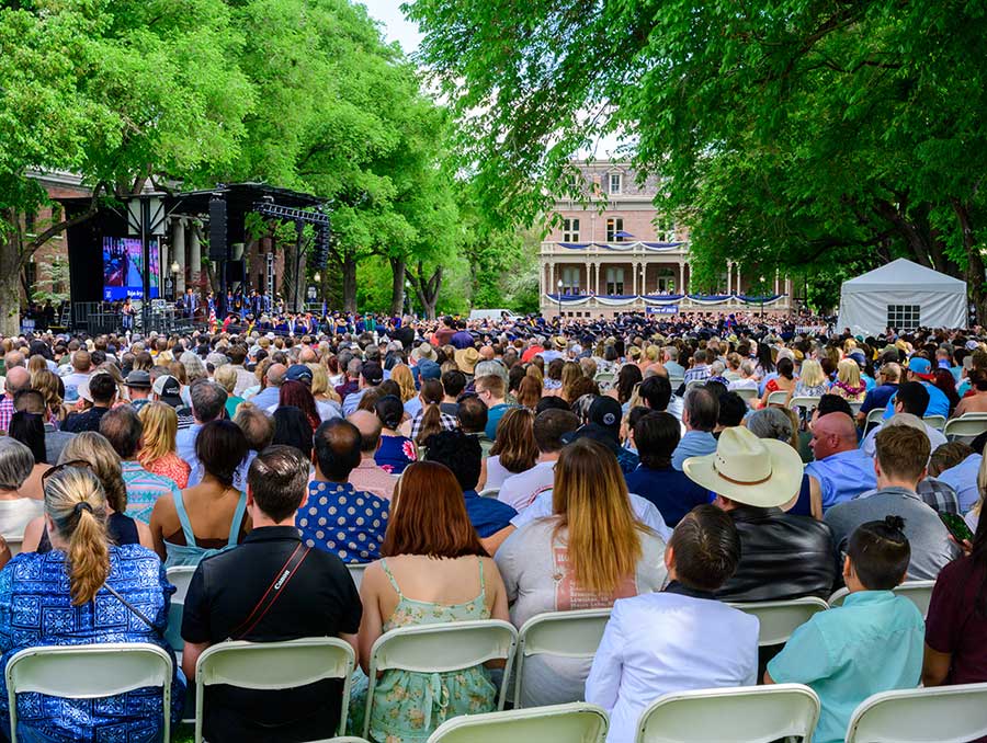 Beyond a sea of proud families are graduates in academic regalia walking across the commencement stage under the shade of the towering deciduous trees which line the University's historic quad.