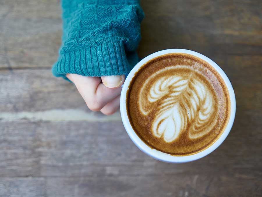 A hand holds a full coffee mug by the handle above a wooden table