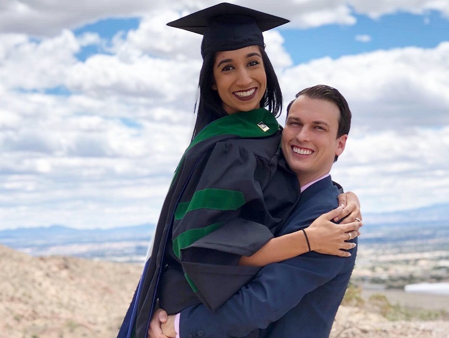 Aradhana Mehta and Lance Horner posing for a cute photo in which Aradhana is being held up in her medical school graduation attire by Lance, who is in a suit