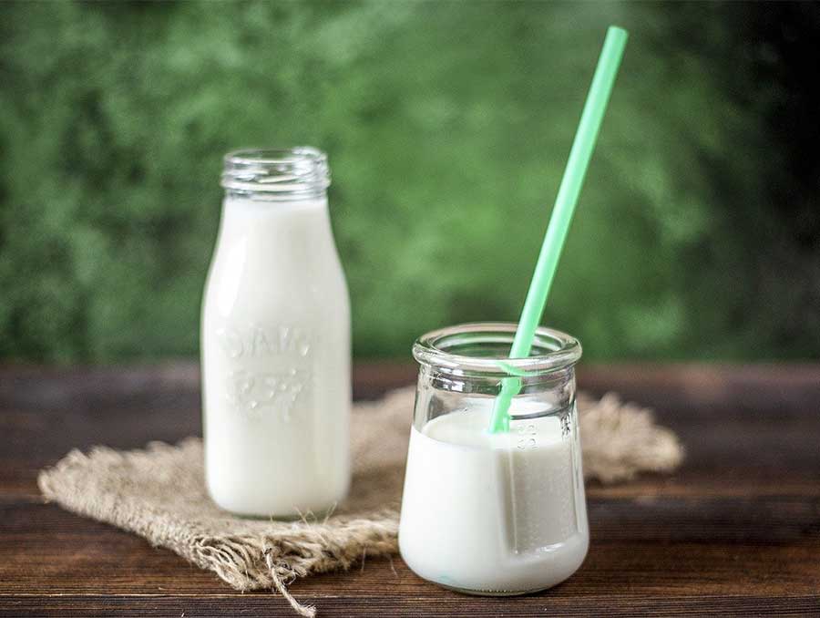 A bottle of milk and a glass of milk with a brightly colored straw sitting on a wooden table