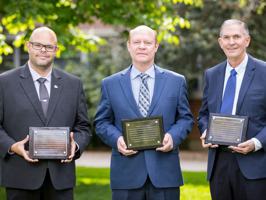 Endowed professors and College dean holding plaques and smiling for photo.