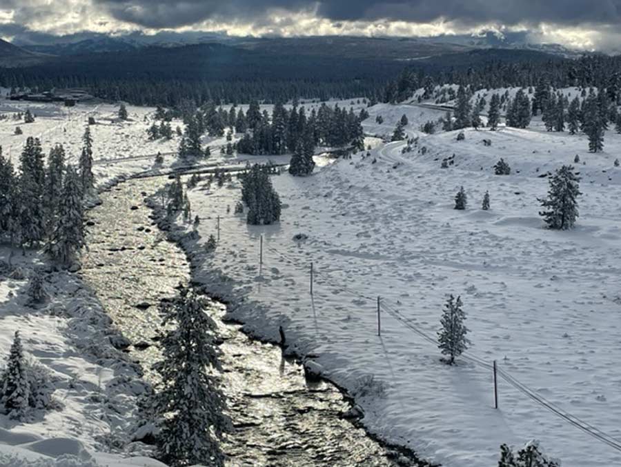 A photo of the Truckee River reaching the tops of the riverbanks. There is snow on the ground all around the river.