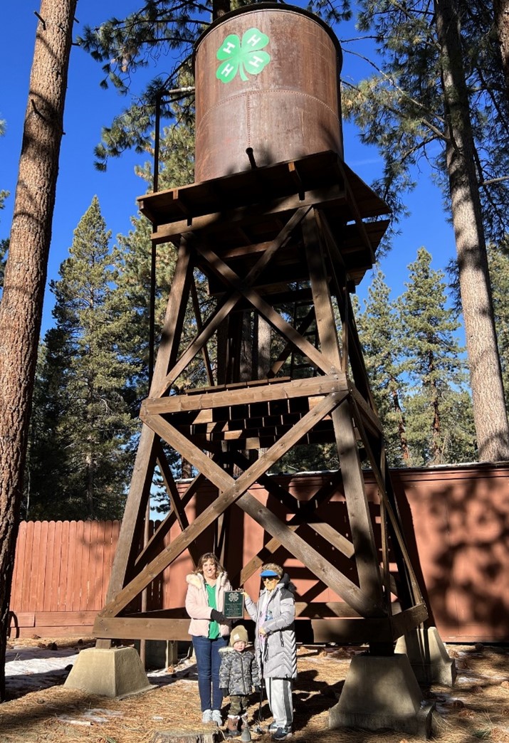 Two adults and a small child standing in front of a watertower.