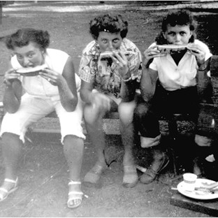 Three people sitting on a log eating food.