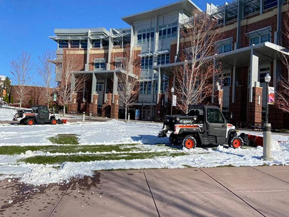 University grounds crew using machinery to remove snow from the lawn in preparation for flag planting