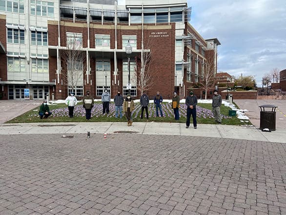 Masked volunteers stand solemnly in the cold with the 2,000 flags they planted for Veteran's Day