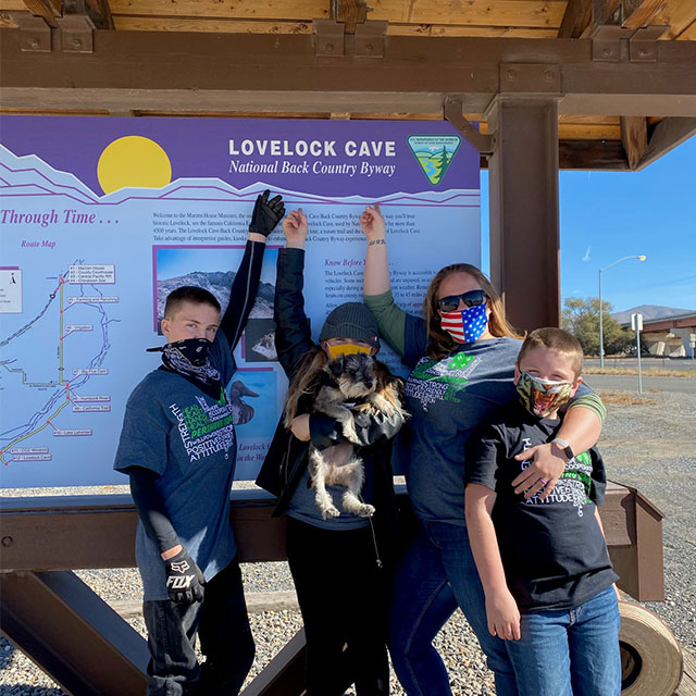 A family wearing 4-H shirts and facemasks points at a sign describing local caves