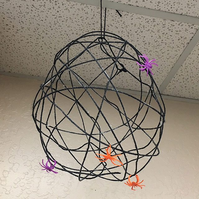 A finished spiderweb adorned with plastic spiders hangs from the ceiling at the Extension office