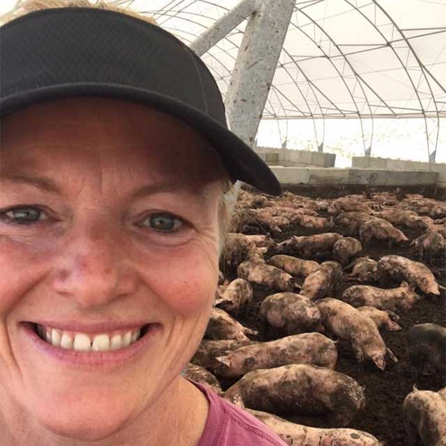 Elizabeth Combs in a greenhouse, smiling and wearing a black ballcap