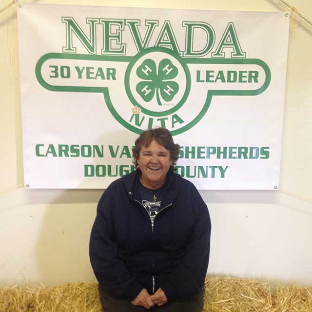 Nita Vick sitting on a hale bale under her 30-year 4-H leader banner