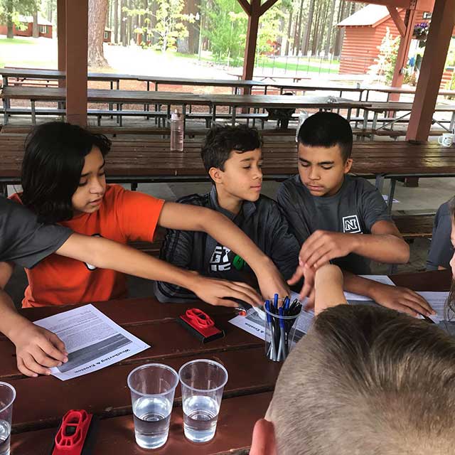 Youth at a table with papers, pens, cups and other supplies