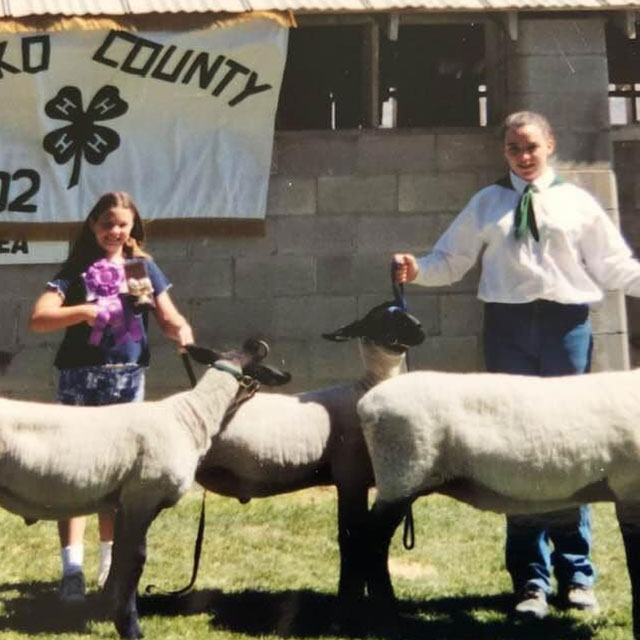 Liz holding a sheep by its tether in front of an Elko County 4-H banner