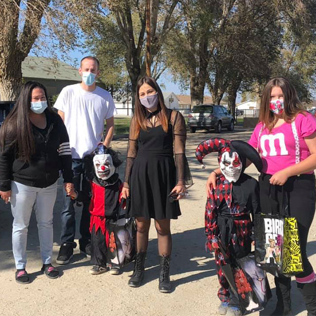 Two families in costume stand six feet apart outside at the Trunk or Treat event