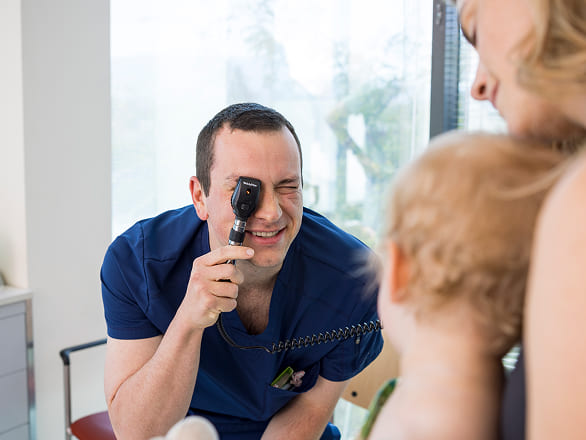 A practitioner prepares for an exam with a baby, being playful to set the baby at ease
