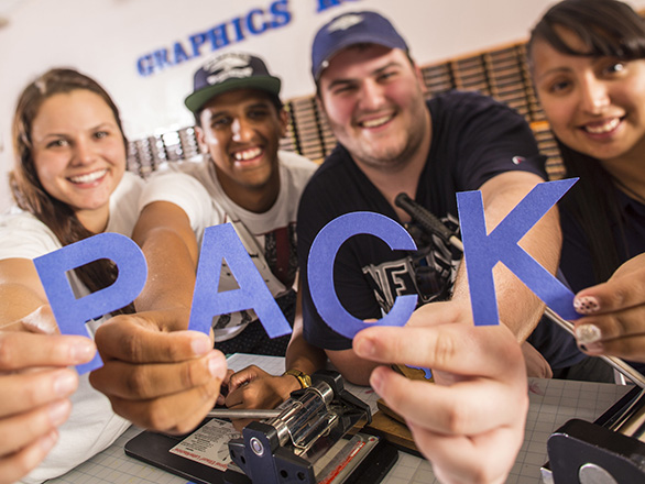 Four smiling students holding cut-out letters that spell "pack."