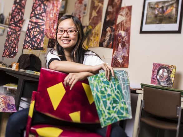 A student sits backward in a chair smiling surrounded by paintings.